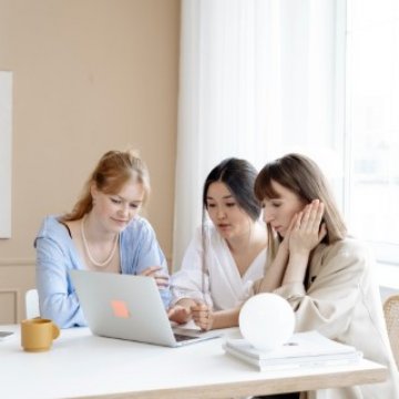 three people sitting around  a desk in an office 